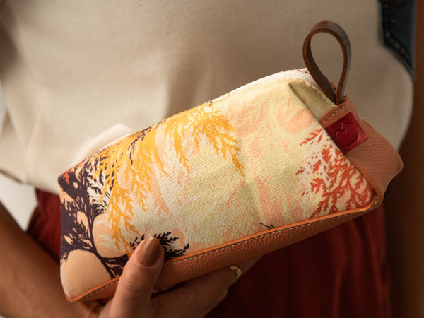 Étui de voyage en cuir peach fuzz et toile imprimée branches de cèdre dans les tons chauds. Fabriqué à Montréal.