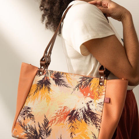 Sac cabas au combo cuir pêche et textile imprimé branches de cèdre aux tons oranges et chauds. Fabriqué à Montréal